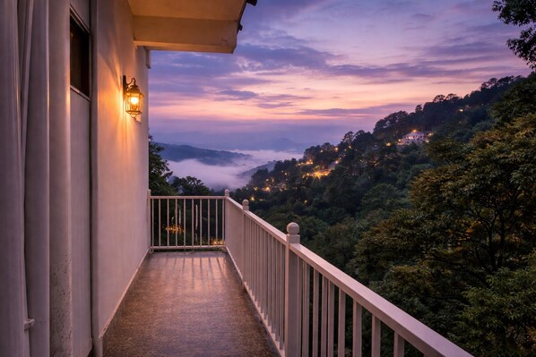 A balcony with a railing, a light fixture, and a view of a forested hillside at dusk. - HOTEL DALHOUSIE VIEW (Dalhousie)