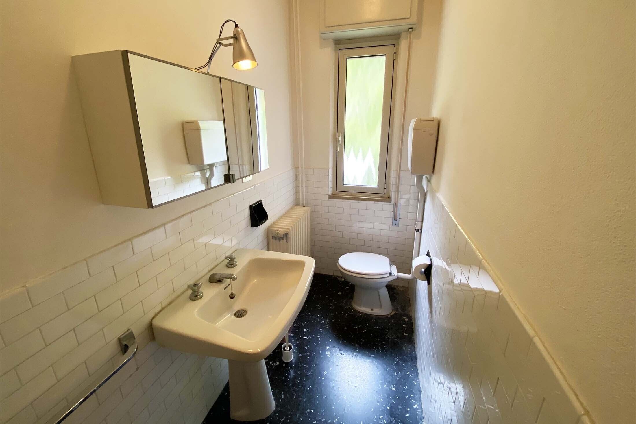 A small bathroom with a white sink, a toilet, a mirror, and a window.