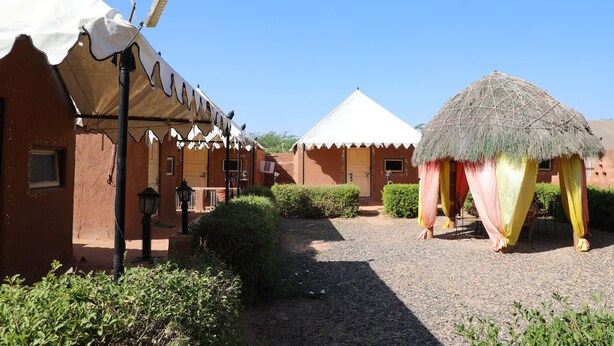 Un patio con una cabaña de techo de paja, un edificio con toldo blanco y una estructura de ladrillo rojo.