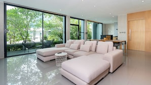 A modern living room with a large sectional sofa, a small round table, and a view of the outdoors through large windows. - Design Duplex P10 in Natural Park Resort (Kamala)