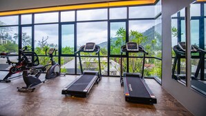 A gym with treadmills and exercise equipment, large windows with a view of greenery and buildings. - Design Duplex P10 in Natural Park Resort (Kamala)