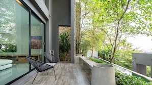 A modern outdoor space with a glass wall, a seating area with chairs, a large planter, and a view of greenery. - Design Duplex P10 in Natural Park Resort (Kamala)