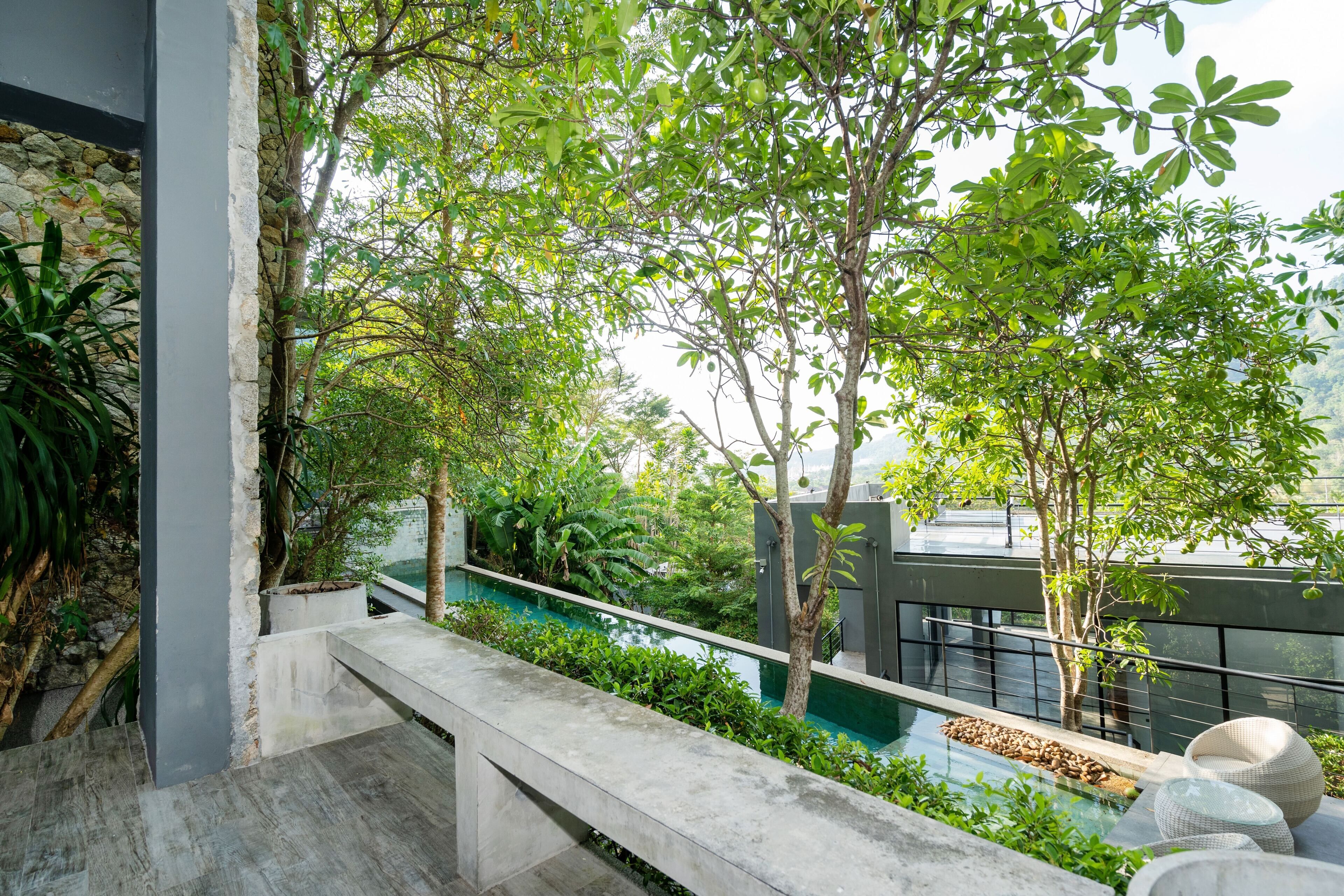 A modern outdoor terrace with a stone wall, a concrete bench, a small water feature, and lush greenery.