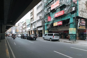 A street with multiple vehicles, including cars and motorcycles, and a building with a fire escape and various signs. - RedDoorz @ Riches Holiday Hotel Avenida (Manila)