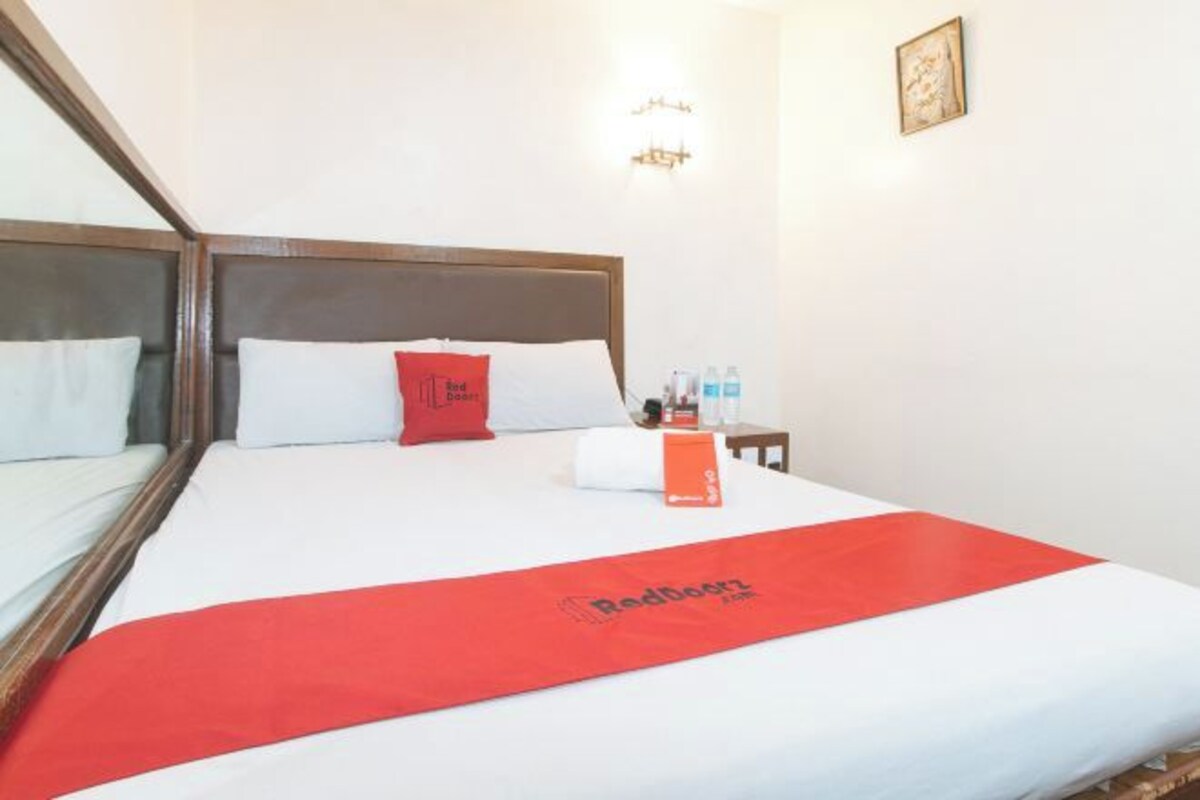 A hotel room with a large bed, a red throw blanket, and a nightstand with toiletries.