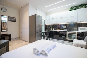 A modern hotel room with a bed, a desk, a kitchen area with a refrigerator, microwave, and sink. - Cozy Studio at Vyronas for 2 pers by MPS (Vironas)