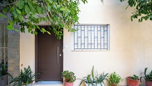 A building entrance with a brown door, a window with metal bars, and several potted plants on the ground. - Cozy Studio at Vyronas for 2 pers by MPS (Vironas)