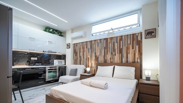 A modern hotel room with a bed, a desk, and a chair. There is a window with a view of the sky. - Cozy Studio at Vyronas for 2 pers by MPS (Vironas)