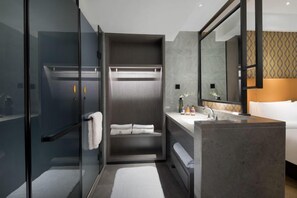Une salle de bain moderne avec une douche à parois de verre, un meuble-lavabo avec un miroir et un lit avec une tête de lit.