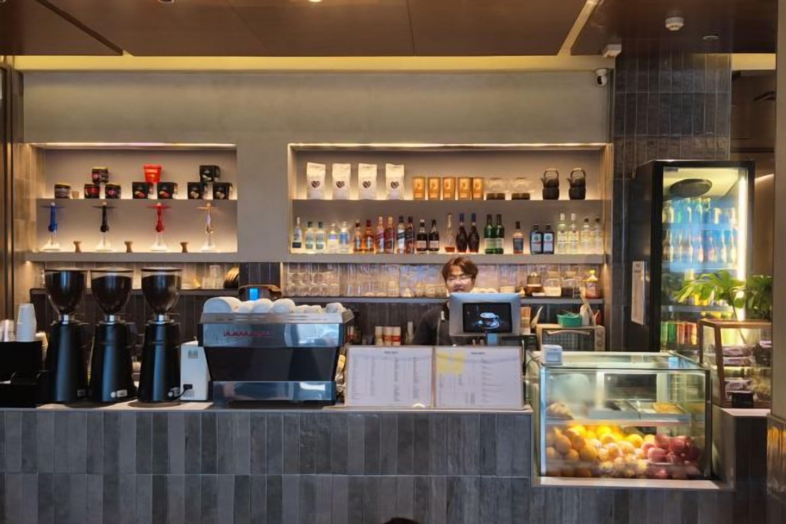 A bar area with coffee machines, shelves of bottles, and a fruit display.