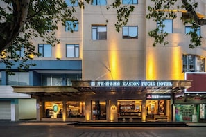 L’entrée d’un hôtel, avec une enseigne indiquant « KASION PUGIS HOTEL », un espace d’entrée abrité et un café Starbucks bien visible.