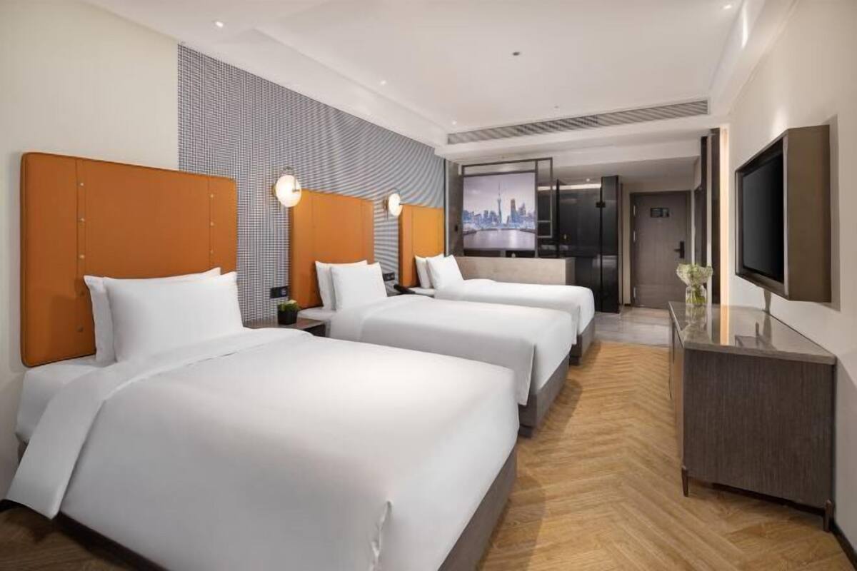 A hotel room with three beds, a TV, and a cityscape view.