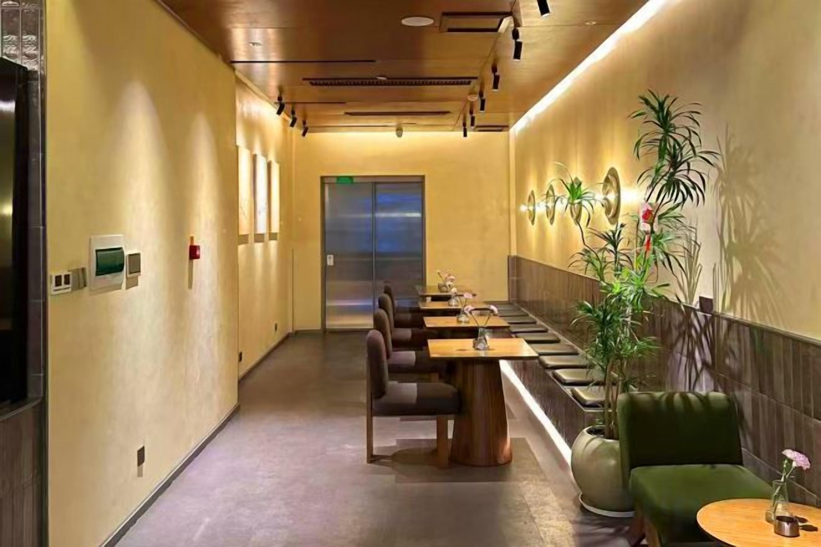 Un pasillo de hotel con una larga mesa y sillas, una recepción y una planta.