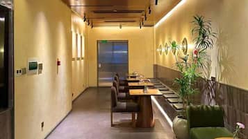 Un pasillo de hotel con una larga mesa y sillas, una recepción y una planta.