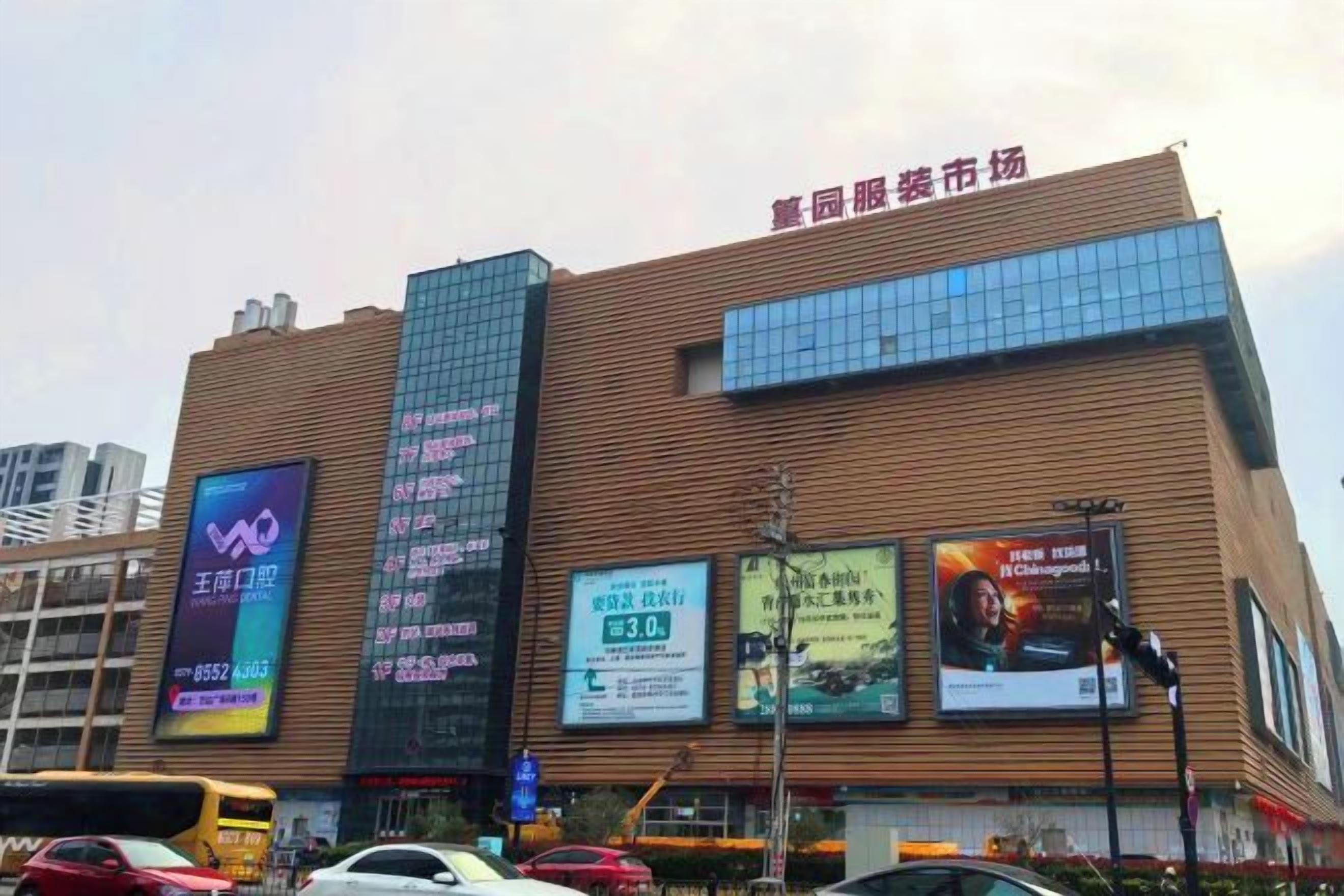 A building with multiple advertisements on its facade, a large sign at the top, and a busy street in front.