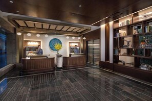 Ein Hotel-Empfangsbereich mit einer Rezeption, einem großen, runden Kunstwerk und einer Bücherwand mit verschiedenen Gegenständen.