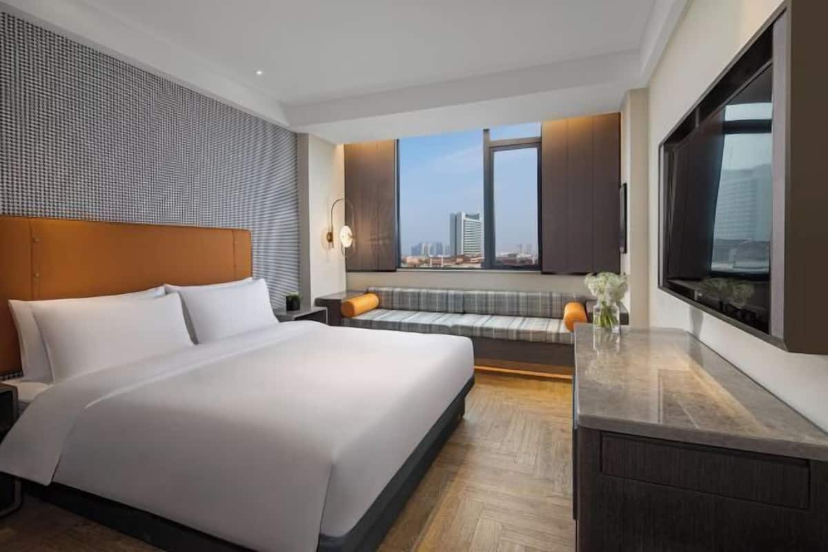 A modern hotel room with a large bed, a seating area with a view, and a large TV on the wall.