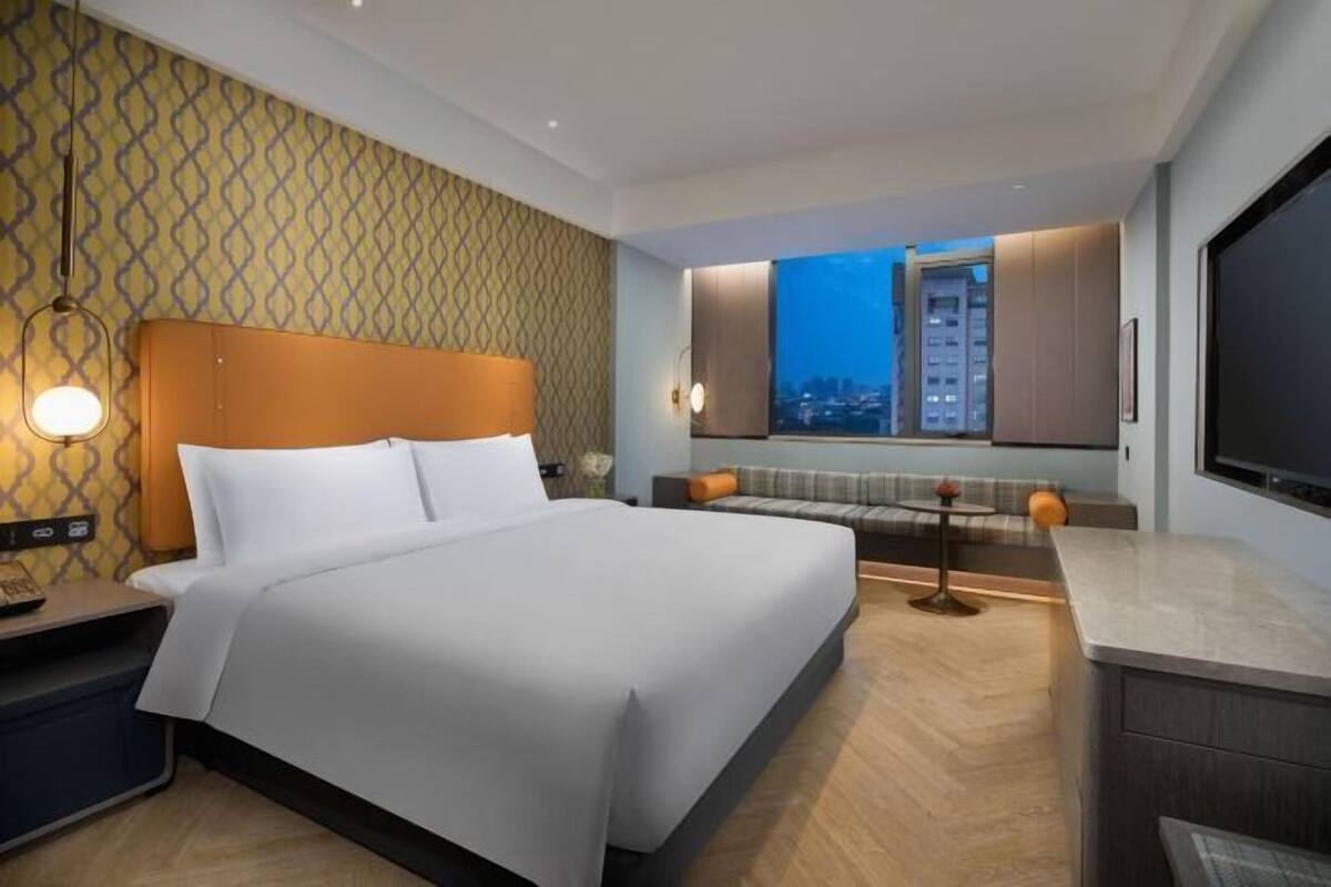 A modern hotel room with a large bed, a seating area with a view, and a flat-screen TV.