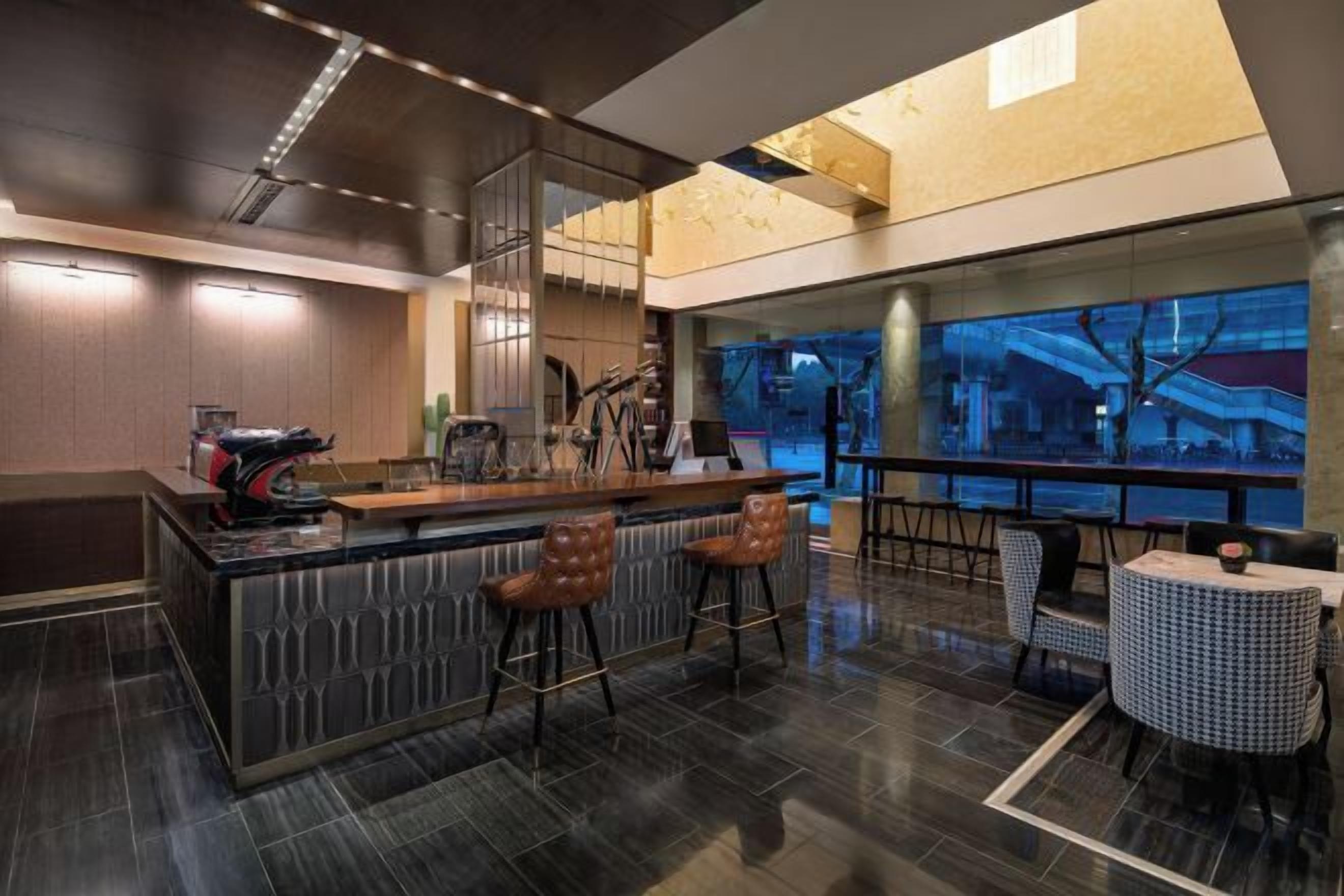 A modern bar area with a high counter, bar stools, and a view of the cityscape through large windows.