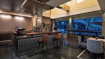 A modern bar area with a high counter, bar stools, and a view of the cityscape through large windows.