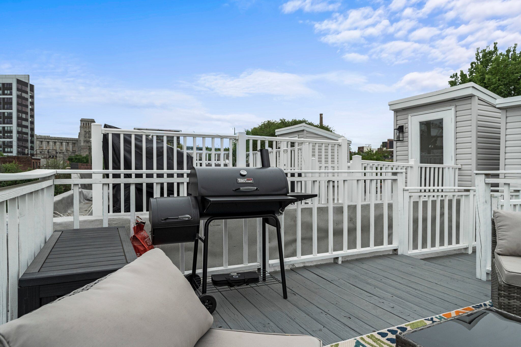 A rooftop deck with a grill, outdoor furniture, and a view of the cityscape.