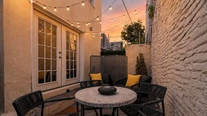 Eine Terrasse mit einem runden Tisch und Stühlen, Lichterketten und einer überdachten Sitzgelegenheit.