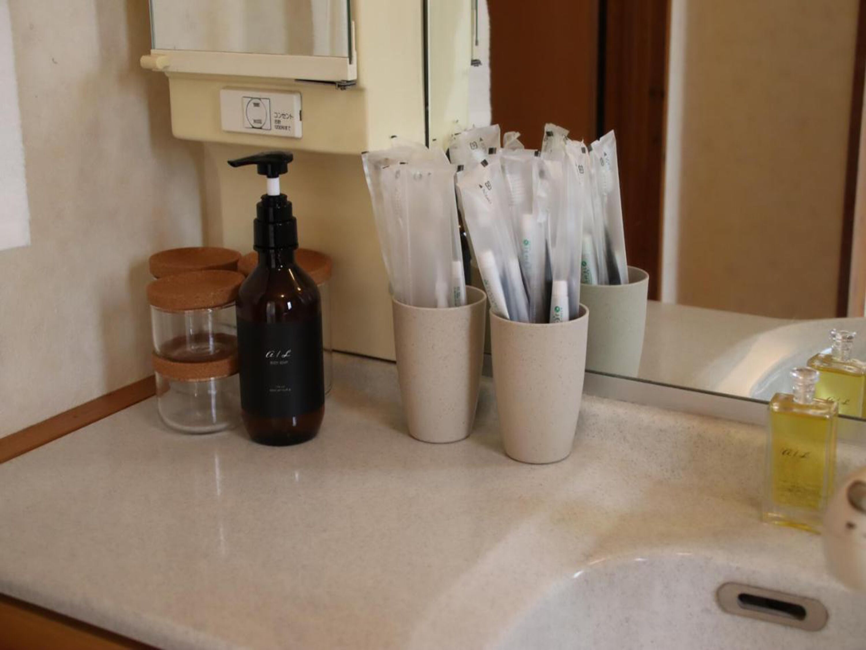 Una encimera de baño con una botella de jabón líquido, un dispensador y varios recipientes de artículos de aseo.