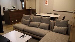 Ein modernes Wohnzimmer mit einer Eckcouch, einem kleinen Tisch, einer Küchenzeile mit Mikrowelle und einem Esstisch mit Stühlen.
