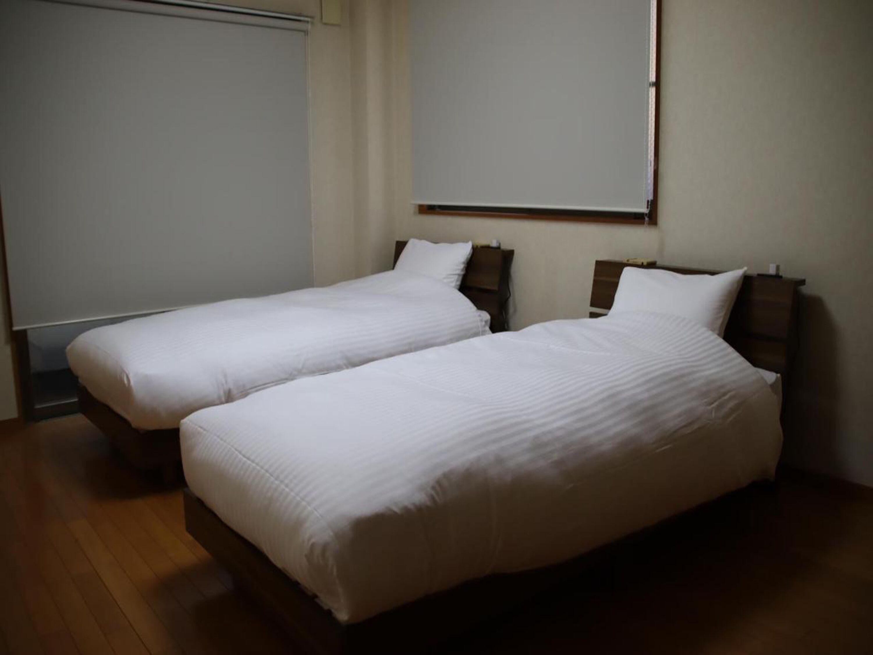 Ein Zimmer mit zwei Einzelbetten, Holzkopfteilen, einer weißen Wand und einem Holzboden.