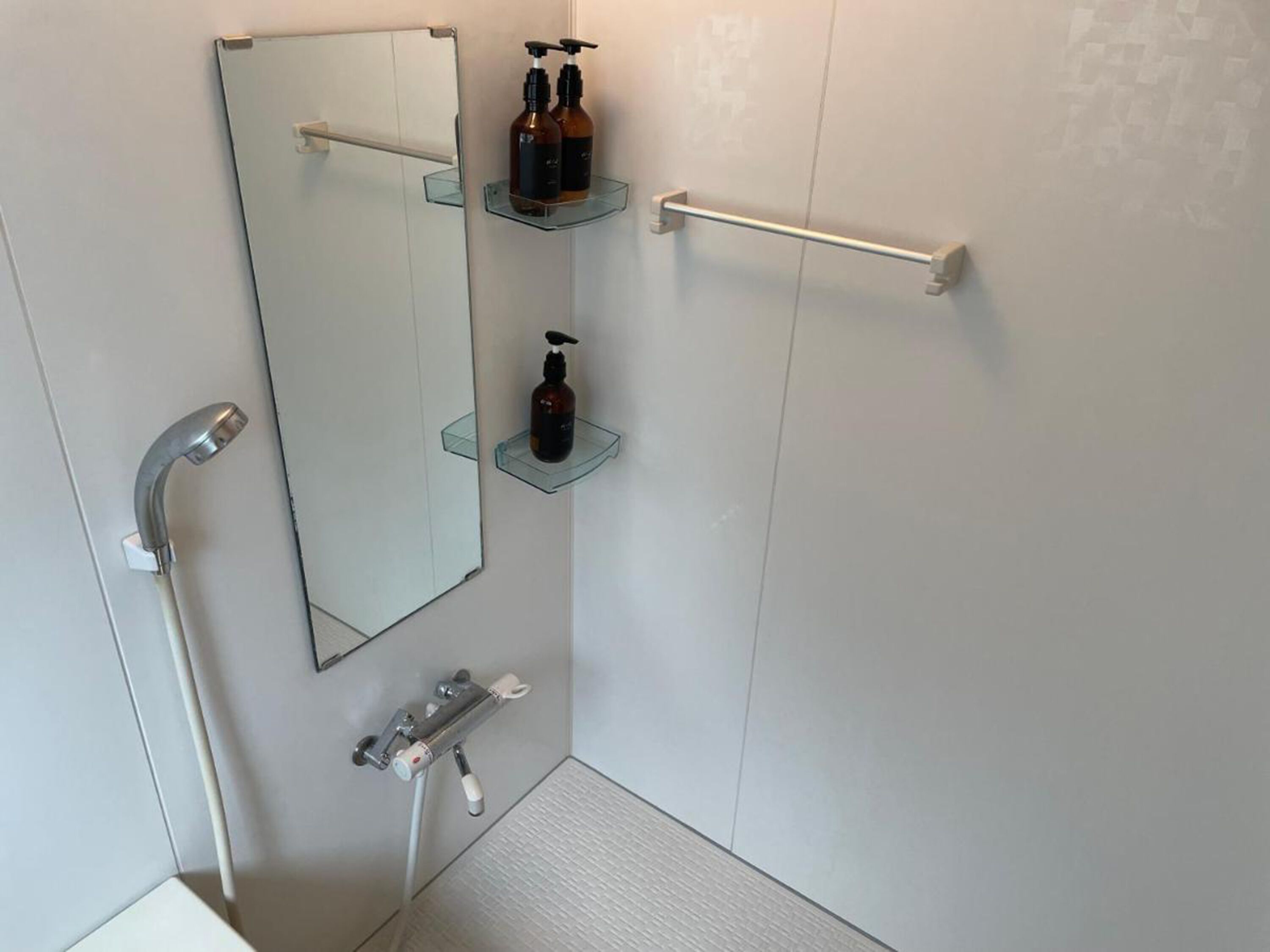 Un baño moderno con cabina de ducha de vidrio, ducha de mano, toallero y dos repisas de vidrio con artículos de aseo.