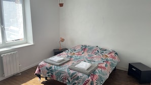 A bedroom with a bed, a nightstand, a lamp, a radiator, and a window. - Charming house in the heart of the village (Bazouges-la-Pérouse)