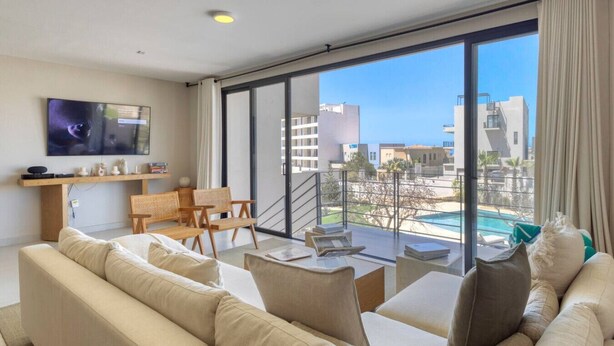 Una sala de estar moderna con un ventanal grande, un televisor de pantalla plana y vista a una piscina.