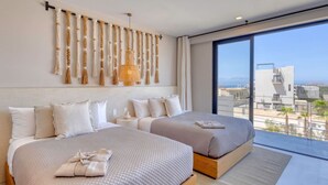 Una habitación de hotel moderna con dos camas, un ventanal grande con vistas a la ciudad y un tapiz decorativo de macramé.
