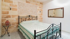 A bedroom with a brick-patterned wall, a bed with a patterned bedspread, a bedside table with a vase, and a mirror on the wall. - 4163 Abate Filippo Home Holiday by Barbarhouse (Nardò)