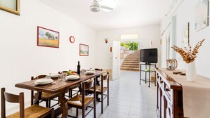 A dining area with a wooden table and chairs, a TV on a stand, and a staircase leading to an outdoor area. - 4163 Abate Filippo Home Holiday by Barbarhouse (Nardò)
