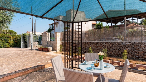 A covered outdoor seating area with wicker chairs and a table set for dining, surrounded by a stone wall and a blue mesh canopy. - 4163 Abate Filippo Home Holiday by Barbarhouse (Nardò)