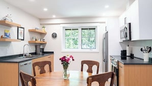A modern kitchen with wooden cabinets, a dining table with chairs, a vase with flowers, and a window with greenery outside. - The Cedar Suite - Secluded Mountain Retreat with Forest Views and Hot Tub (Revelstoke)