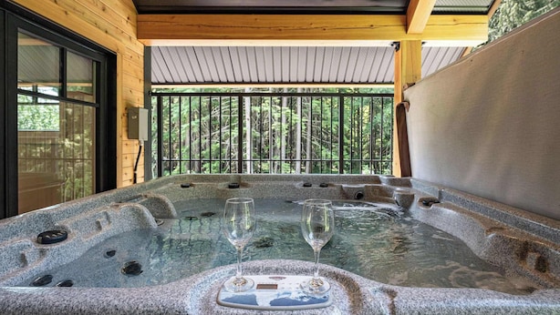 A hot tub with two glasses, surrounded by wooden walls and a view of trees. - The Cedar Suite - Secluded Mountain Retreat with Forest Views and Hot Tub (Revelstoke)