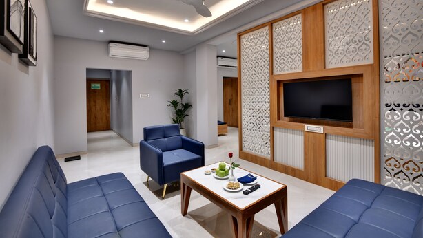 Ein modernes Wohnzimmer mit einem blauen Sofa, einem Couchtisch mit Vase und Fernbedienung sowie einem an einer Holzpaneelwand montierten Fernseher.