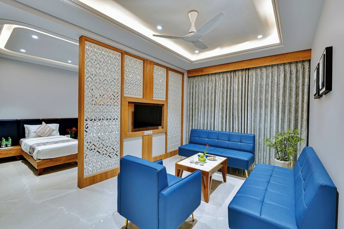 Ein modernes Hotelzimmer mit Bett, blauem Sofa, Holztisch und Fernseher.