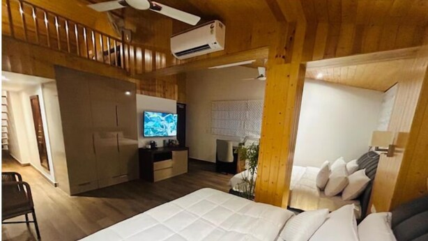 A hotel room with a large bed, a desk with a flat-screen TV, a ceiling fan, and wooden walls. - Eminence the Corbett (Ramnagar)