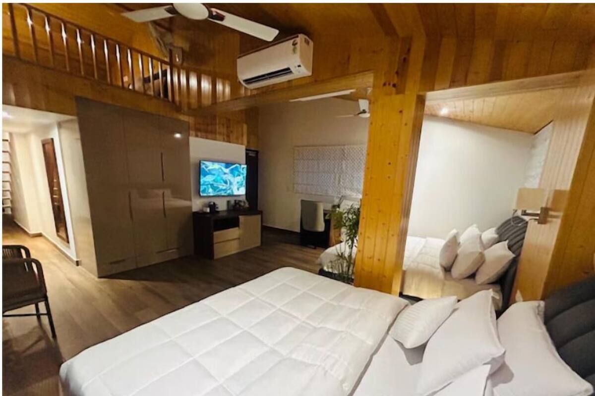 A hotel room with a large bed, a desk with a flat-screen TV, a ceiling fan, and wooden walls.