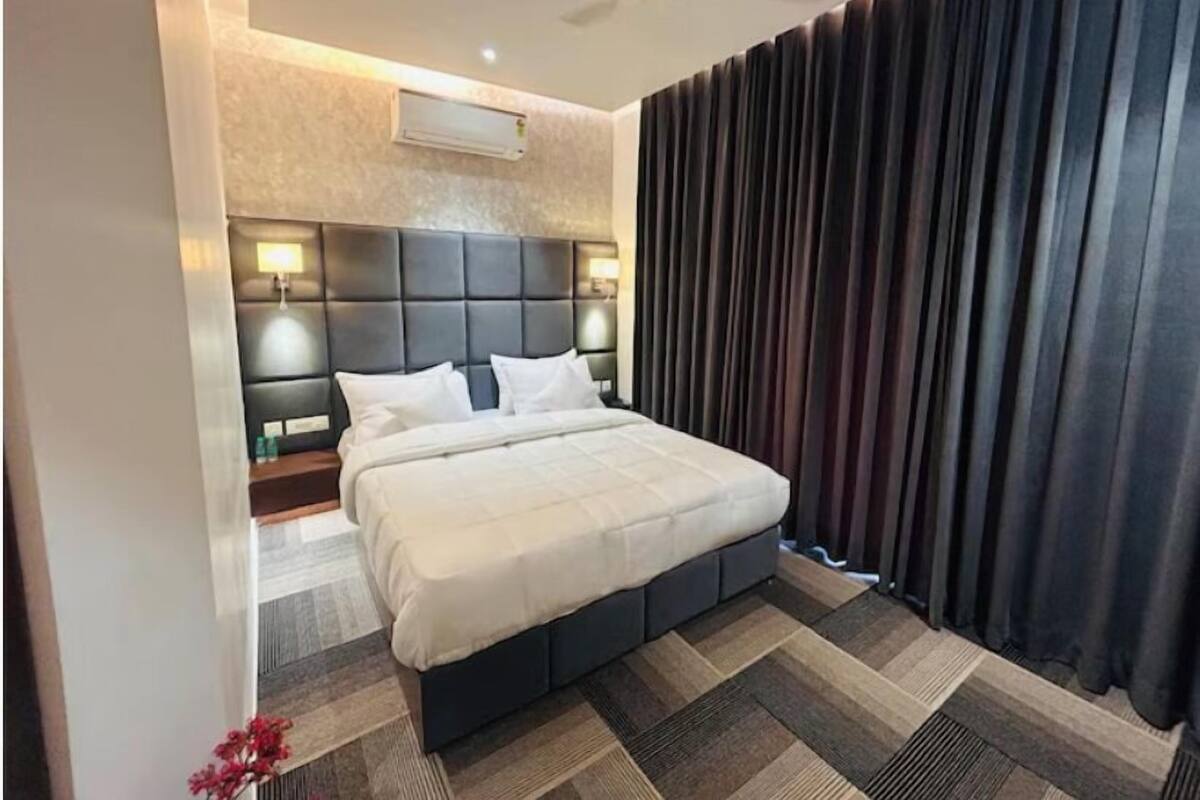 A modern hotel room with a large bed, a headboard with built-in lighting, a ceiling fan, and a dark curtain on the window.