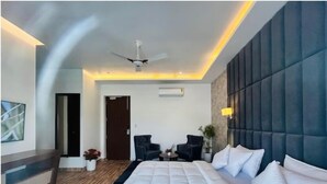 A modern hotel room with a large bed, two armchairs, a small table, and a ceiling fan. - Eminence the Corbett (Ramnagar)