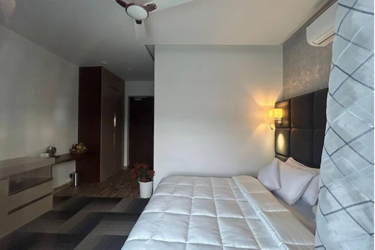 A modern hotel room with a bed, a ceiling fan, a bedside lamp, and a view of the hallway.