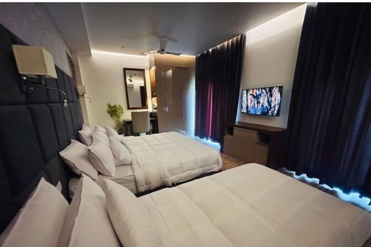 A hotel room with two beds, a TV, a desk, and a chair.