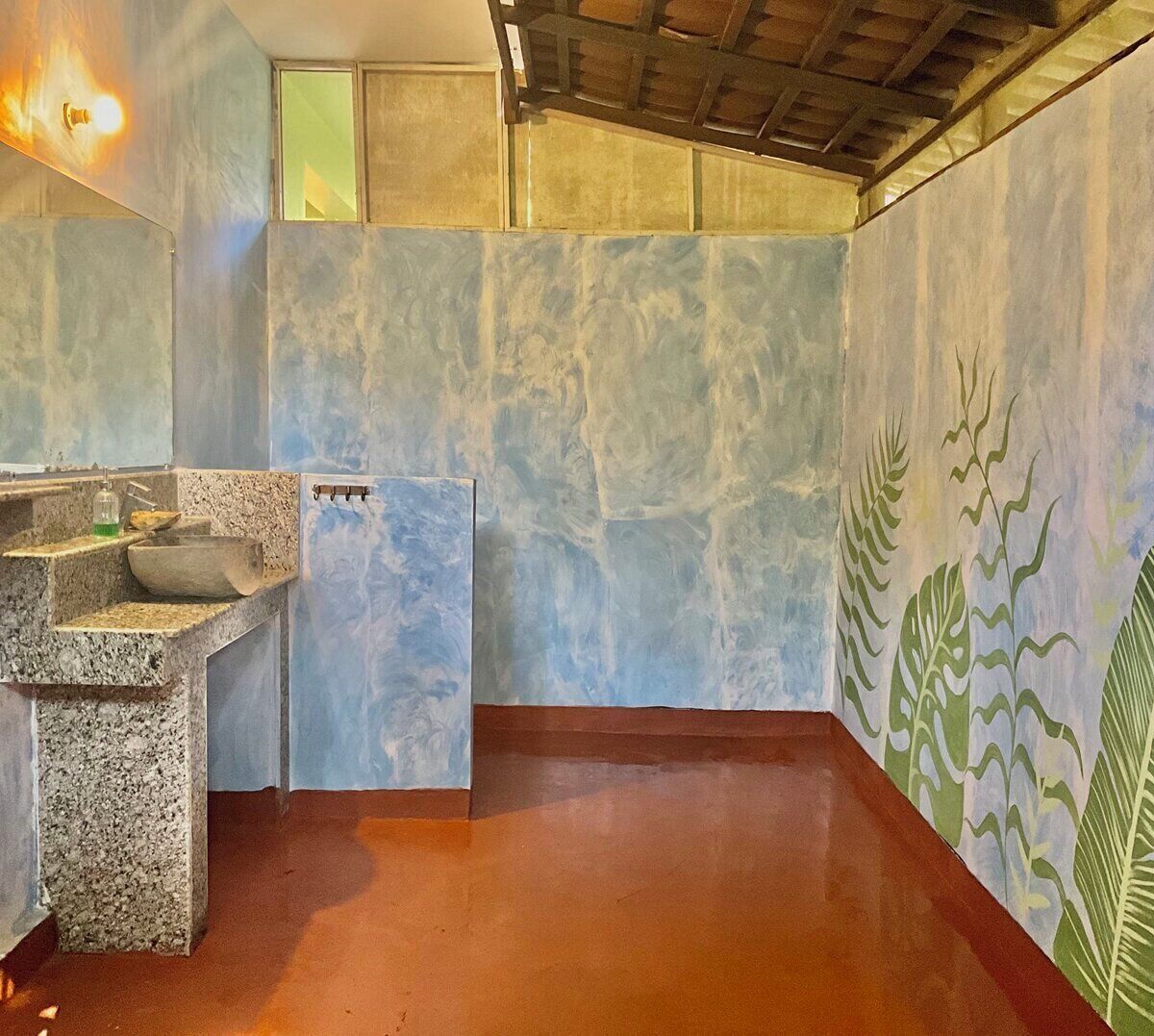 A bathroom with a stone sink, a mirror, and a wall with a leaf pattern.