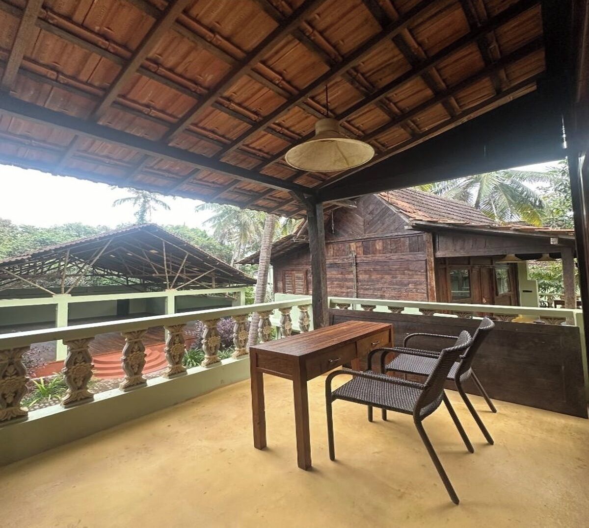 Un espacio al aire libre techado con una mesa y sillas, techo de paja y vistas a un edificio tradicional.