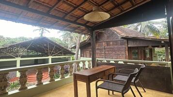 Un espacio al aire libre techado con una mesa y sillas, techo de paja y vistas a un edificio tradicional.