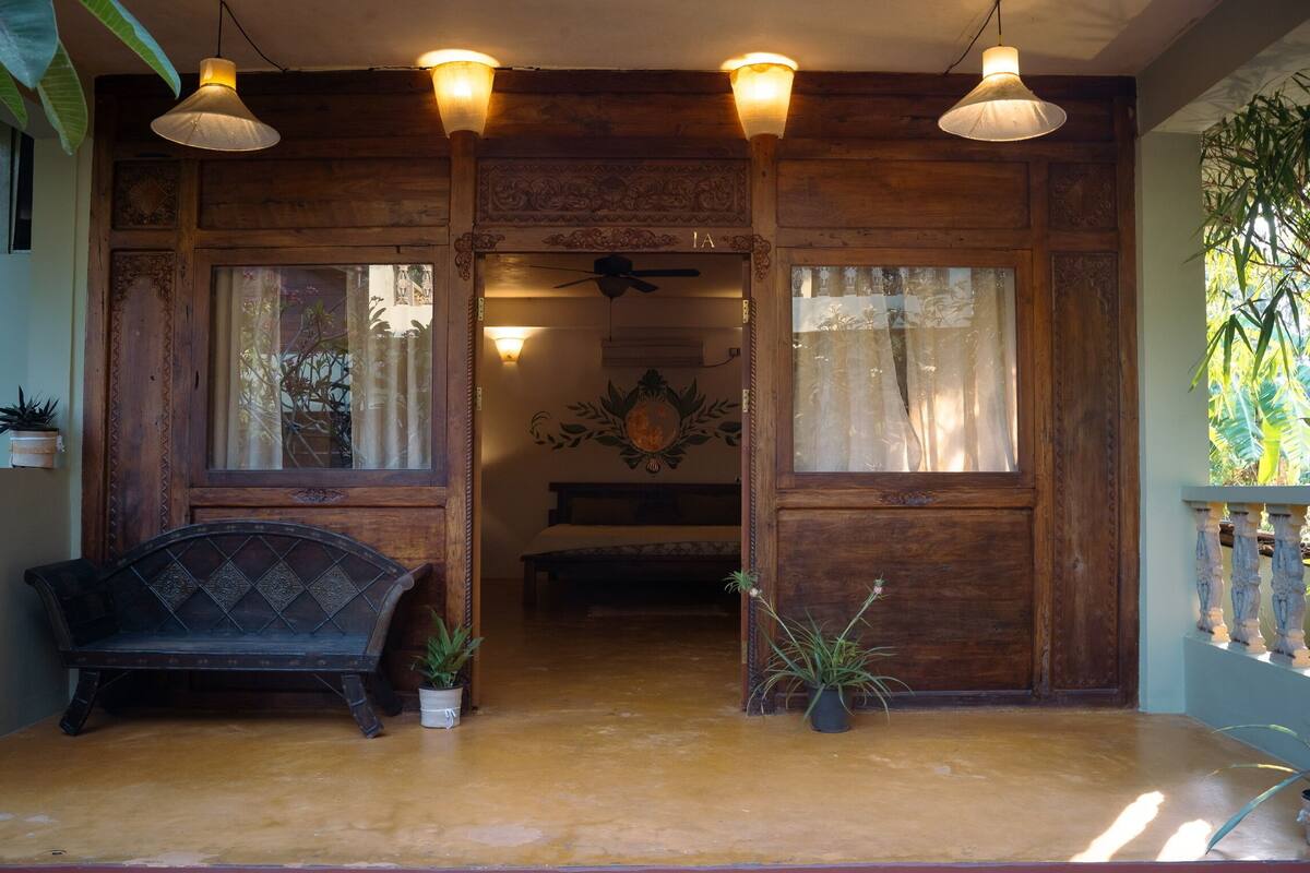 A wooden entryway with a bench, potted plants, and a bed in the background.